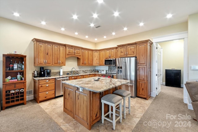 kitchen featuring light stone countertops, sink, stainless steel appliances, a breakfast bar area, and a kitchen island