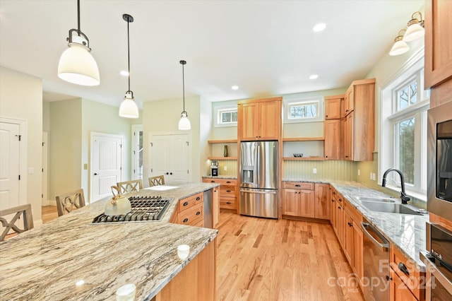 kitchen with light stone counters, stainless steel appliances, sink, light hardwood / wood-style floors, and hanging light fixtures