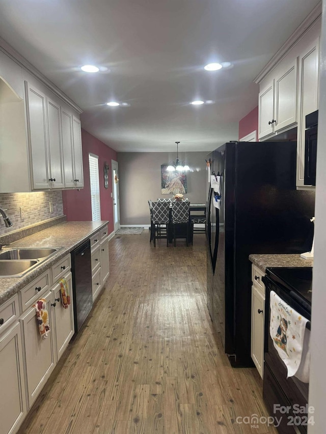 kitchen featuring sink, pendant lighting, light hardwood / wood-style floors, decorative backsplash, and black appliances