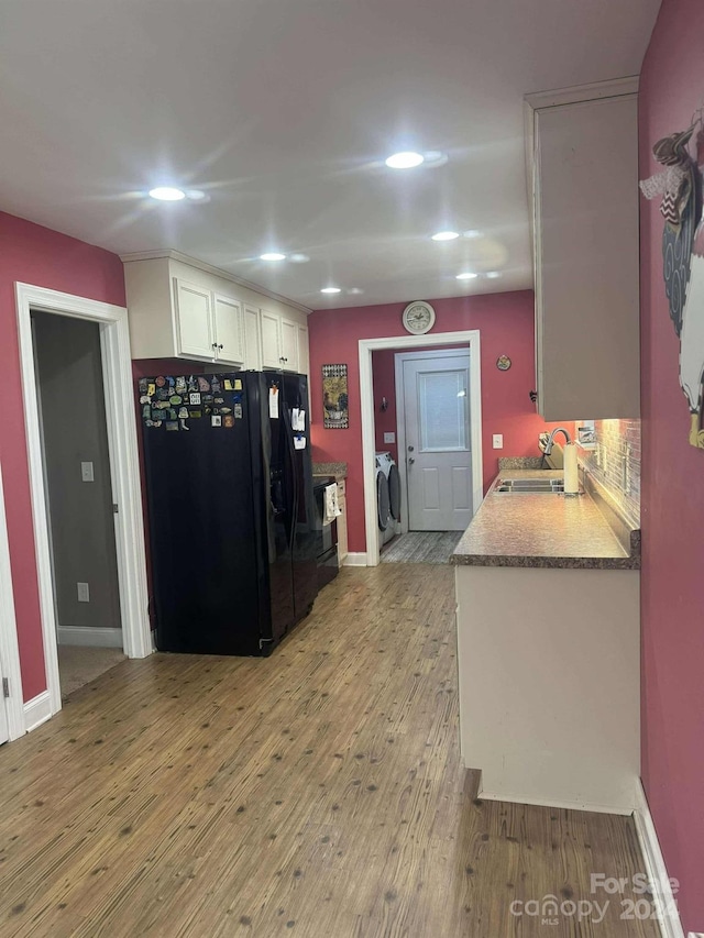 kitchen with washing machine and clothes dryer, white cabinetry, sink, light hardwood / wood-style floors, and black fridge with ice dispenser