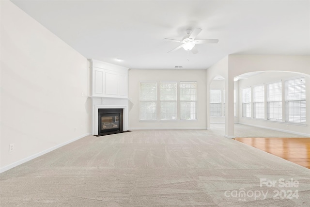 unfurnished living room featuring ceiling fan, light colored carpet, and a wealth of natural light