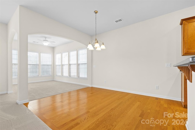 unfurnished dining area featuring ceiling fan with notable chandelier and light hardwood / wood-style floors