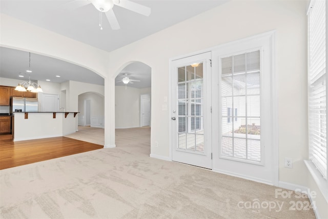 unfurnished living room with ceiling fan with notable chandelier and light colored carpet