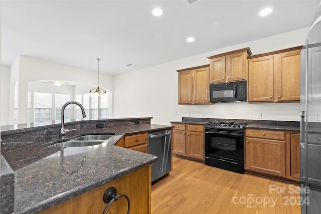 kitchen featuring dark stone counters, black appliances, sink, decorative light fixtures, and light hardwood / wood-style floors