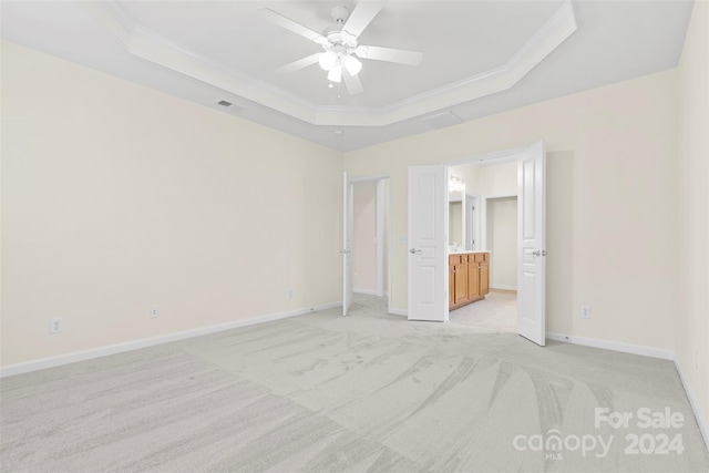 unfurnished bedroom with a raised ceiling, ensuite bath, ceiling fan, and light carpet