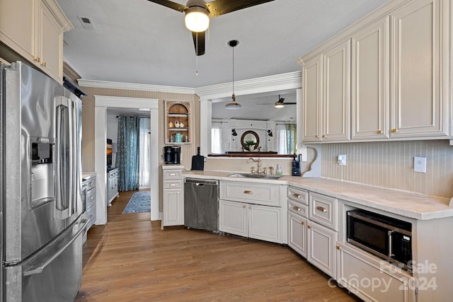 kitchen with ornamental molding, stainless steel appliances, sink, decorative light fixtures, and light hardwood / wood-style floors