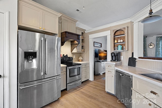 kitchen with appliances with stainless steel finishes, ornamental molding, light hardwood / wood-style flooring, cream cabinetry, and hanging light fixtures