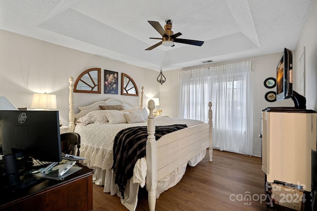 bedroom with a textured ceiling, a raised ceiling, ceiling fan, and dark wood-type flooring