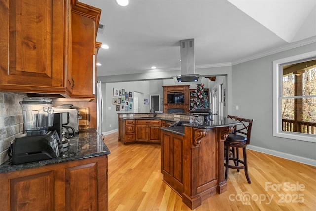 kitchen with dark stone countertops, sink, island range hood, and a breakfast bar