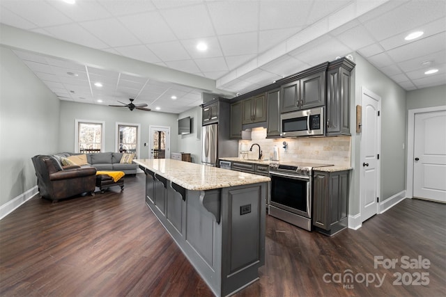 kitchen featuring appliances with stainless steel finishes, a kitchen island, dark hardwood / wood-style floors, tasteful backsplash, and a kitchen bar