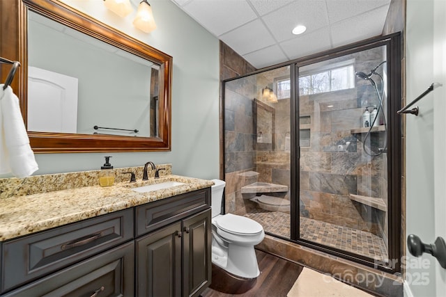 bathroom with hardwood / wood-style flooring, an enclosed shower, vanity, a drop ceiling, and toilet