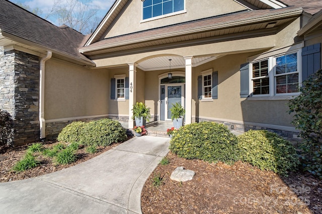 view of exterior entry featuring stone siding, a porch, and stucco siding
