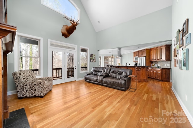 living area with light wood finished floors, baseboards, and high vaulted ceiling