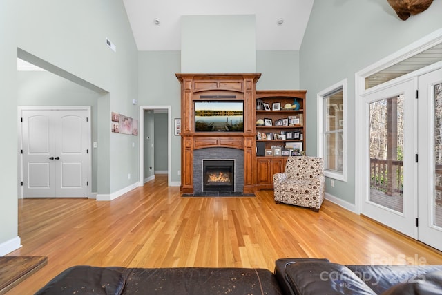 living room featuring visible vents, high vaulted ceiling, light wood-style floors, and a tiled fireplace