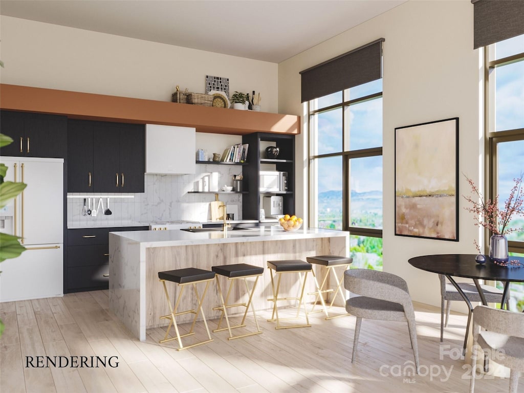 kitchen featuring a breakfast bar, backsplash, white fridge with ice dispenser, an island with sink, and light hardwood / wood-style floors