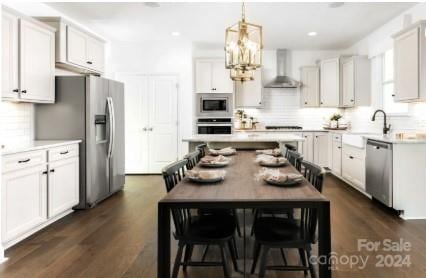 kitchen with stainless steel appliances, a kitchen island, white cabinetry, and wall chimney range hood