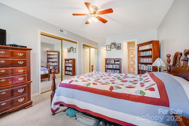 carpeted bedroom with ceiling fan, multiple closets, and a textured ceiling