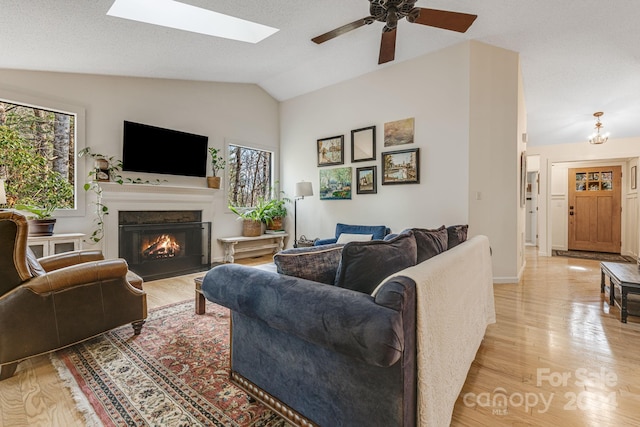 living room with a textured ceiling, light hardwood / wood-style floors, ceiling fan, and vaulted ceiling with skylight