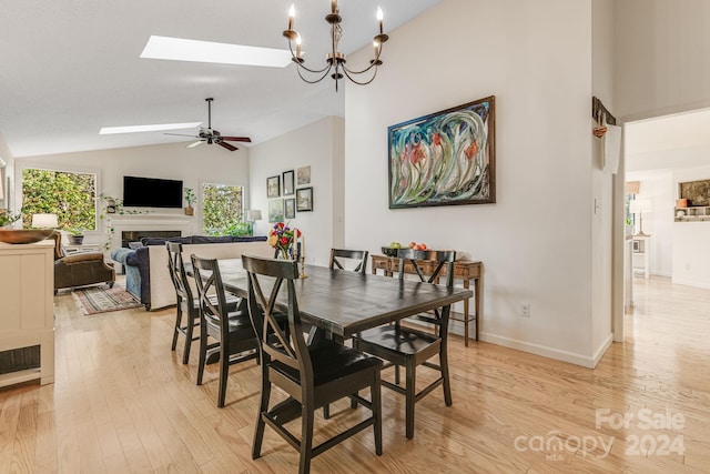 dining room featuring vaulted ceiling with skylight, ceiling fan with notable chandelier, and light hardwood / wood-style flooring