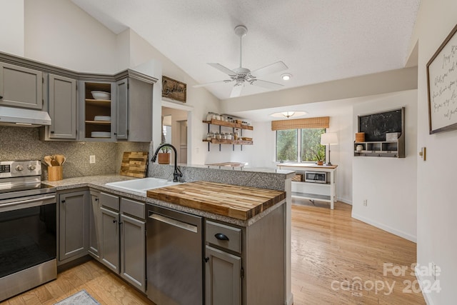 kitchen with kitchen peninsula, appliances with stainless steel finishes, sink, gray cabinets, and lofted ceiling