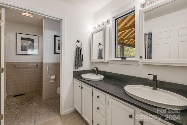 bathroom featuring a textured ceiling, vanity, toilet, and tile walls