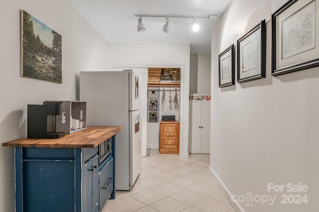 kitchen featuring blue cabinetry, wood counters, white fridge, track lighting, and light tile patterned floors