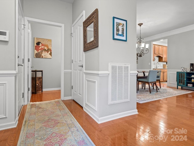 hallway with light hardwood / wood-style floors, an inviting chandelier, and ornamental molding