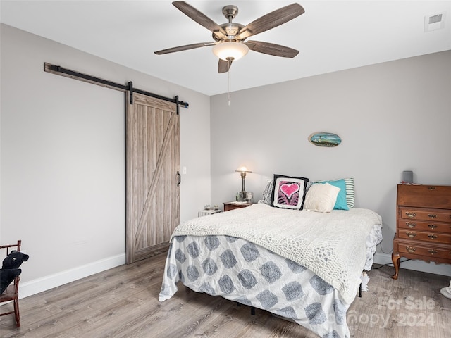 bedroom with ceiling fan, a barn door, and wood-type flooring