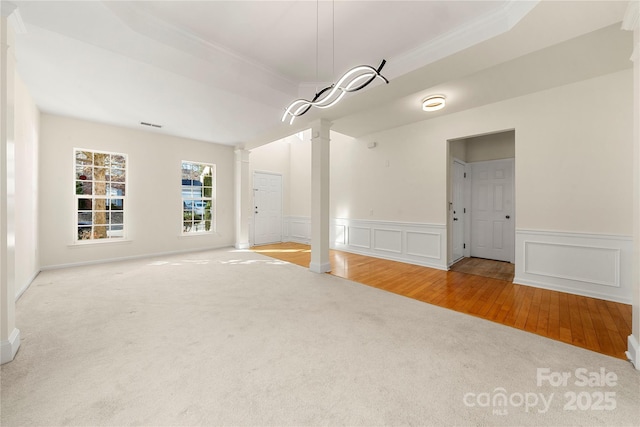 empty room featuring a raised ceiling, light carpet, decorative columns, and ornamental molding