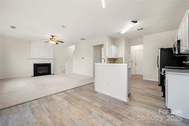 kitchen featuring white cabinets, a fireplace, ceiling fan, stove, and light hardwood / wood-style flooring