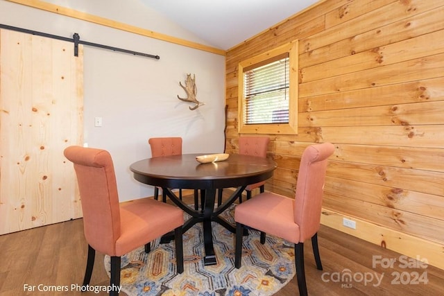 dining area with hardwood / wood-style flooring, a barn door, wood walls, and vaulted ceiling