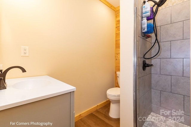 bathroom with wood-type flooring, vanity, a tile shower, and toilet