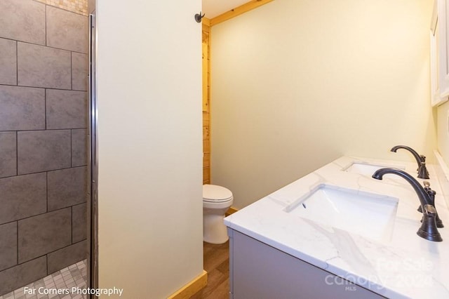 bathroom featuring a tile shower, vanity, wood-type flooring, and toilet