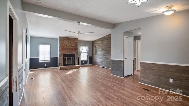 unfurnished living room featuring lofted ceiling with beams, ceiling fan, a textured ceiling, a fireplace, and wood-type flooring