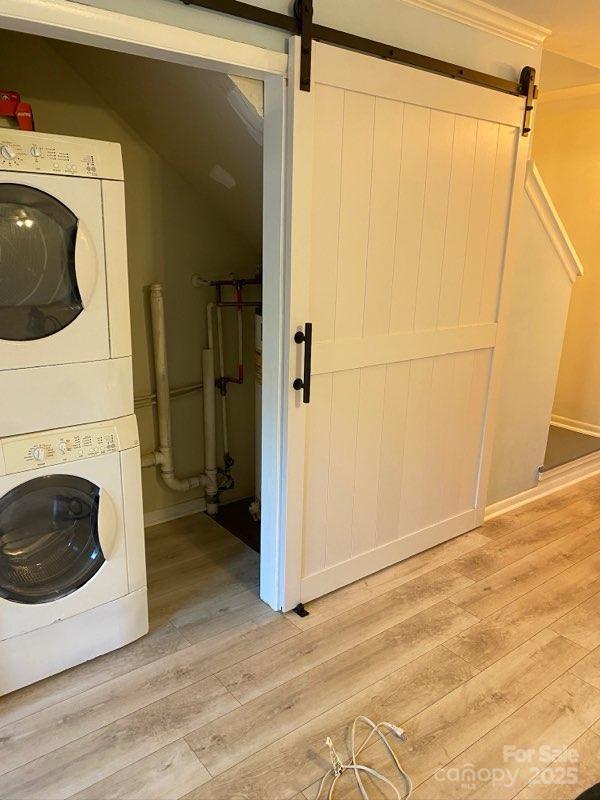 clothes washing area with stacked washer / dryer, light hardwood / wood-style floors, and a barn door