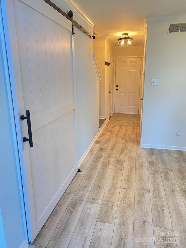 hall with a barn door, crown molding, and light hardwood / wood-style flooring