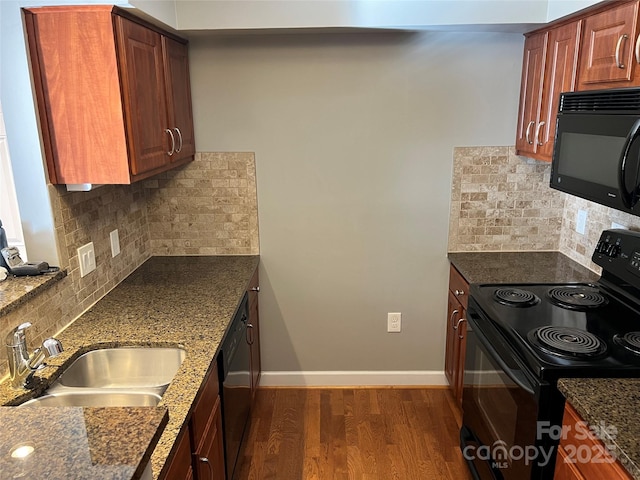 kitchen featuring baseboards, dark wood finished floors, dark stone counters, black appliances, and a sink