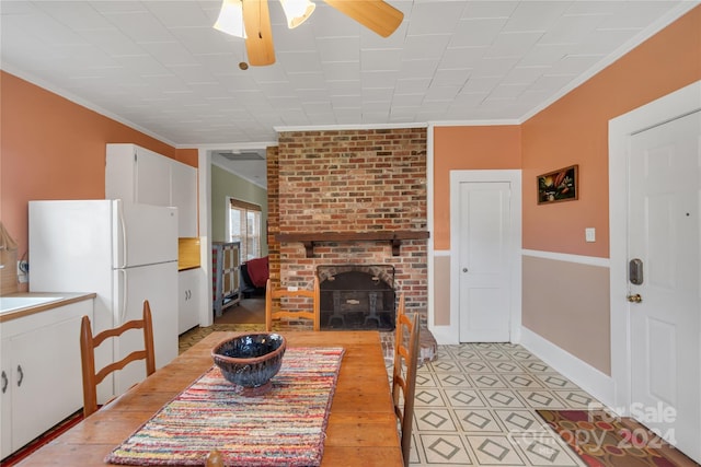 dining space with ceiling fan, sink, a brick fireplace, crown molding, and light wood-type flooring