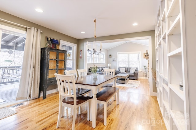 dining area with vaulted ceiling, an inviting chandelier, and light hardwood / wood-style flooring