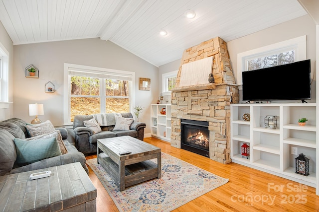 living room with wood-type flooring, a stone fireplace, and vaulted ceiling with beams