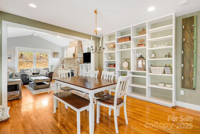 dining area with an inviting chandelier, vaulted ceiling with beams, a stone fireplace, and wood-type flooring