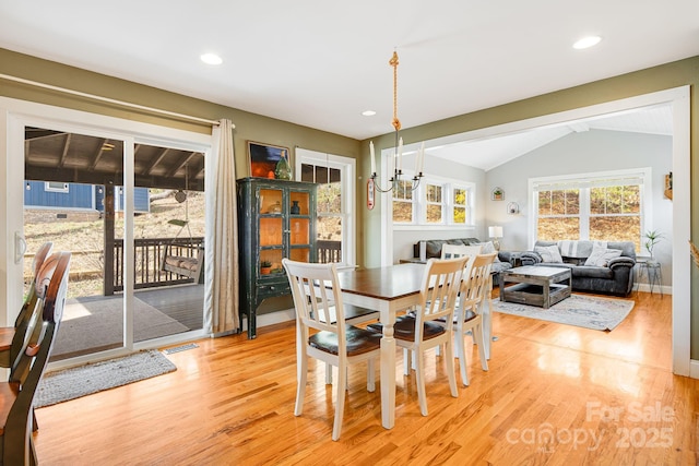 dining space featuring a chandelier, vaulted ceiling, and light wood-type flooring