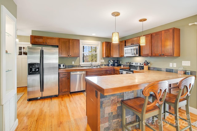 kitchen featuring hanging light fixtures, a kitchen breakfast bar, stainless steel appliances, light hardwood / wood-style floors, and kitchen peninsula