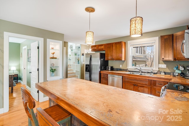 kitchen featuring sink, appliances with stainless steel finishes, decorative light fixtures, kitchen peninsula, and light wood-type flooring