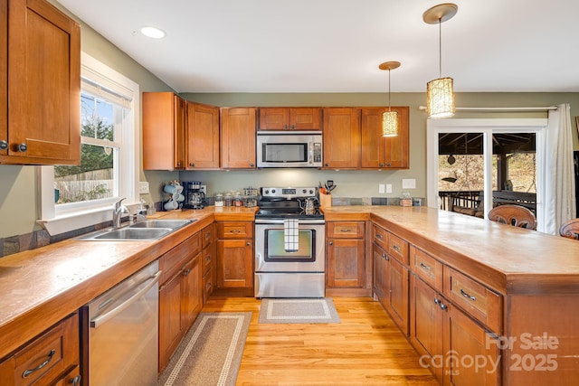 kitchen featuring appliances with stainless steel finishes, sink, pendant lighting, and light hardwood / wood-style flooring