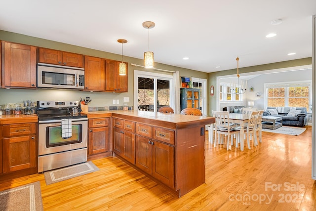 kitchen with stainless steel appliances, kitchen peninsula, light wood-type flooring, and decorative light fixtures