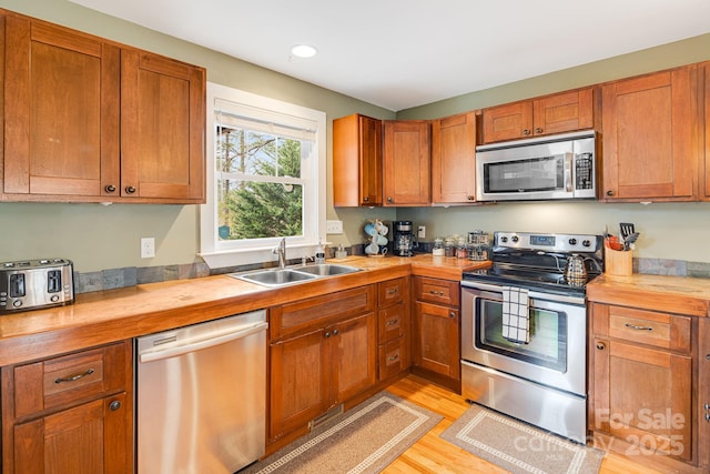 kitchen with stainless steel appliances, light hardwood / wood-style floors, sink, and butcher block countertops