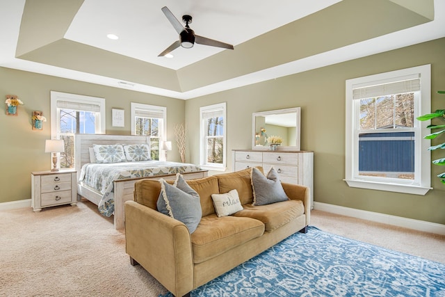 bedroom with light colored carpet, a raised ceiling, and ceiling fan