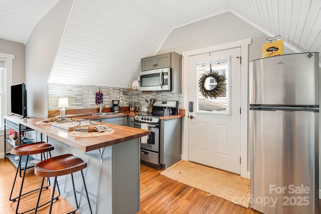 kitchen featuring appliances with stainless steel finishes, wood counters, lofted ceiling, sink, and a breakfast bar area