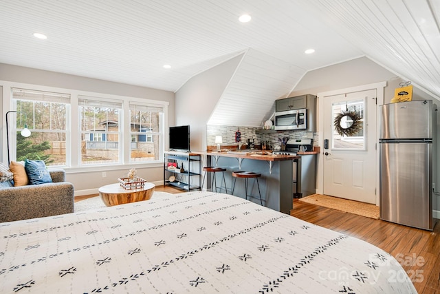 bedroom featuring lofted ceiling, light hardwood / wood-style flooring, and stainless steel refrigerator